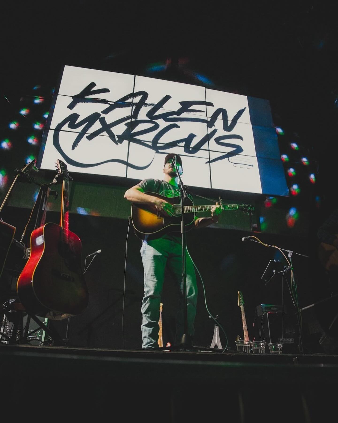 Kalen Mxrcus on stage with guitar and logo backdrop